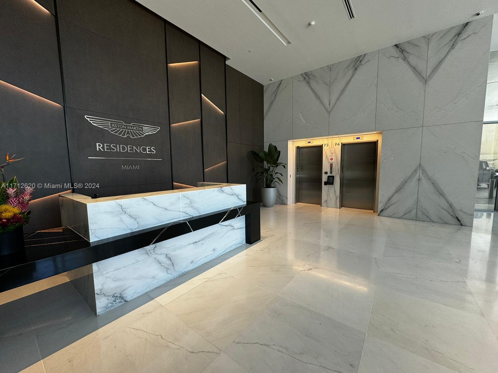 A modern lobby features a marble reception desk, dark paneled walls, and two stainless steel elevators — 300 Biscayne Boulevard Way # 1806, Miami FL 33131, MIAMI, FL