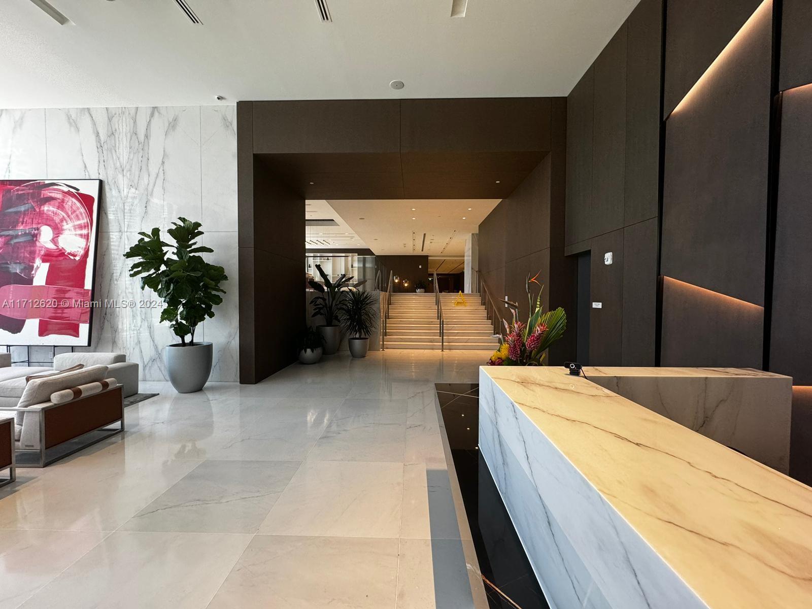 A modern lobby features a marble reception desk, a large abstract painting, and a staircase — 300 Biscayne Boulevard Way # 1806, Miami FL 33131, MIAMI, FL