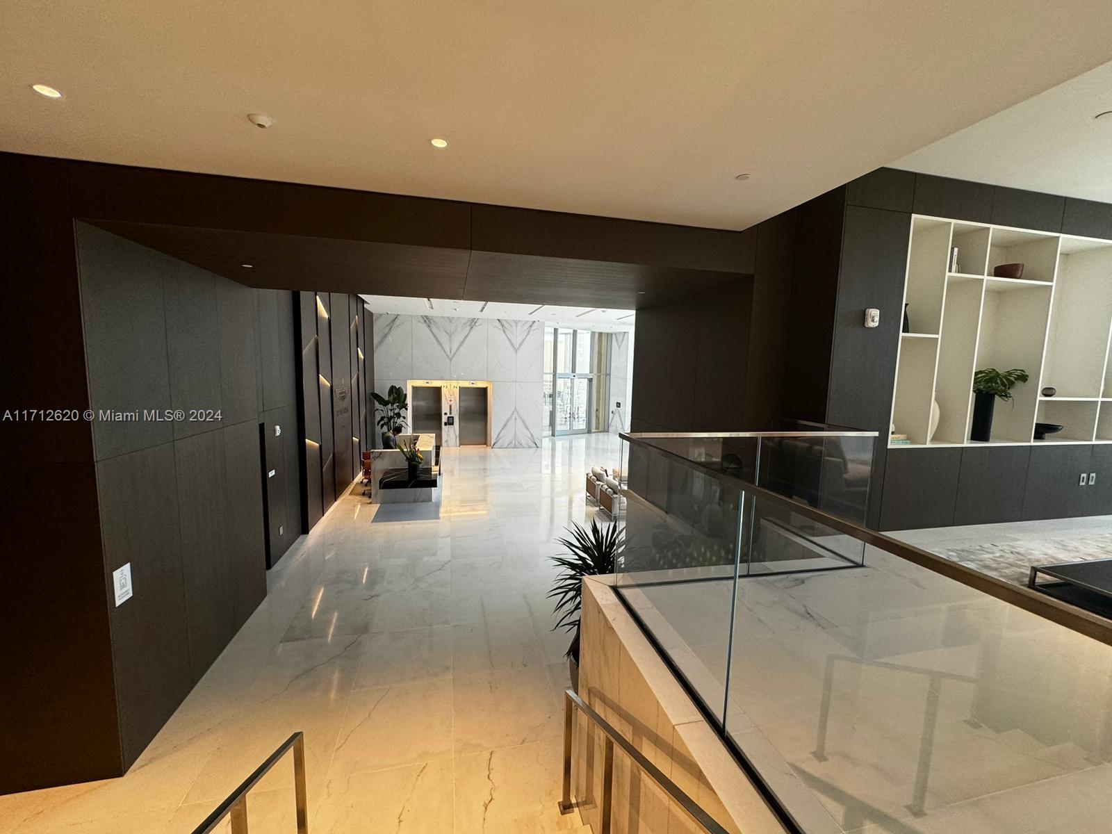 A modern lobby features marble flooring, dark wood paneling, glass railings, and a reception desk — 300 Biscayne Boulevard Way # 1806, Miami FL 33131, MIAMI, FL