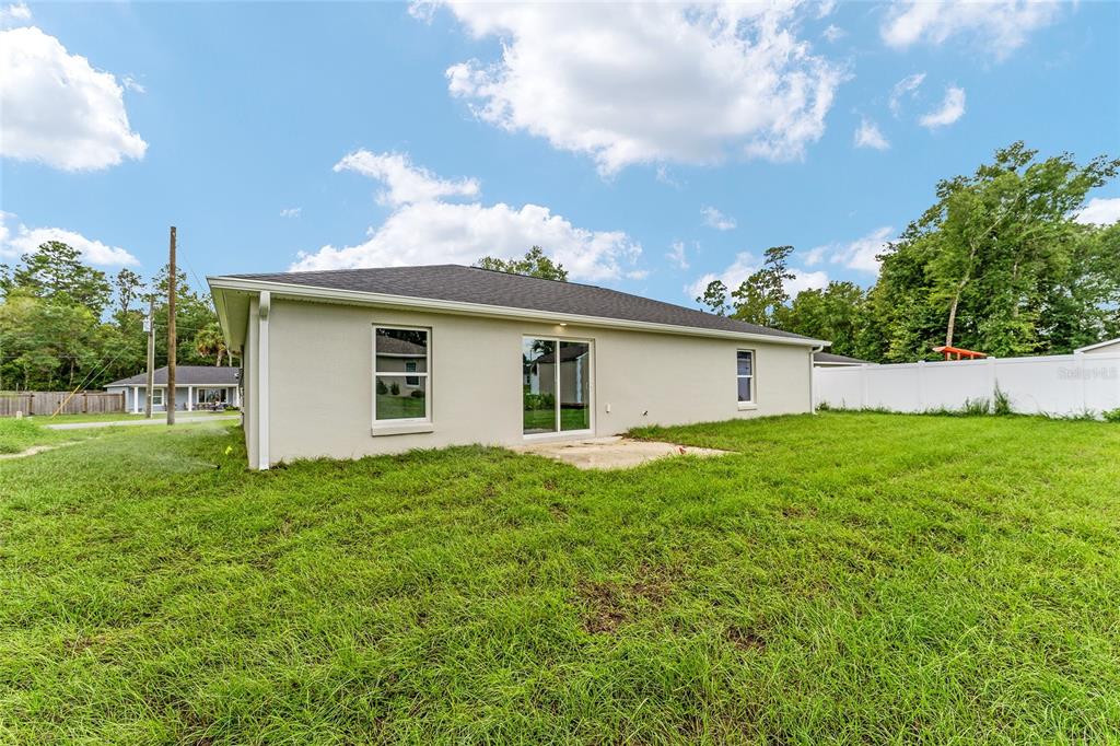 The exterior rear view of a single-story house with a lawn and white vinyl fence — 13027 NE 5TH PLACE, SILVER SPRINGS, FL