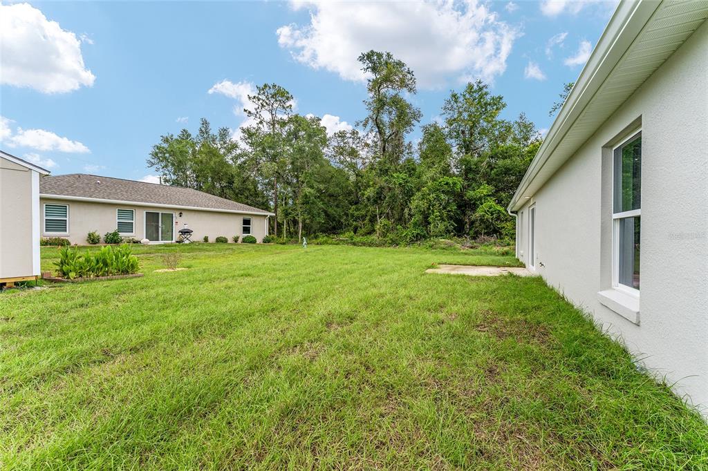A grassy backyard sits between two beige houses with a wooded area in the background — 13027 NE 5TH PLACE, SILVER SPRINGS, FL