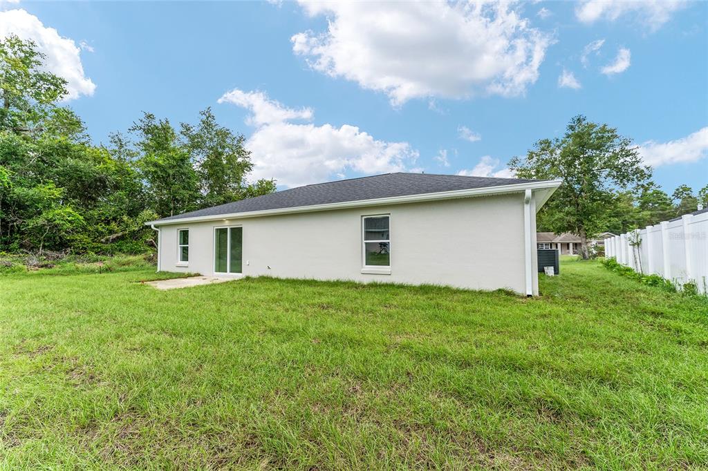 The rear exterior of a single-story house features a concrete patio, sliding doors, and windows — 13027 NE 5TH PLACE, SILVER SPRINGS, FL