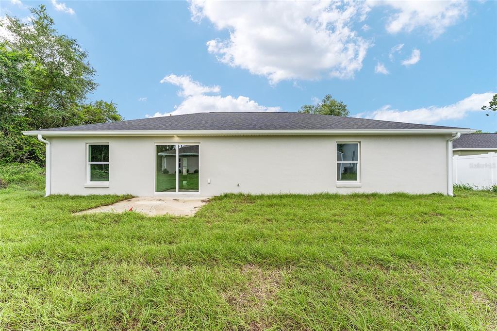 The rear exterior of a single-story house features a concrete patio and sliding glass doors — 13027 NE 5TH PLACE, SILVER SPRINGS, FL