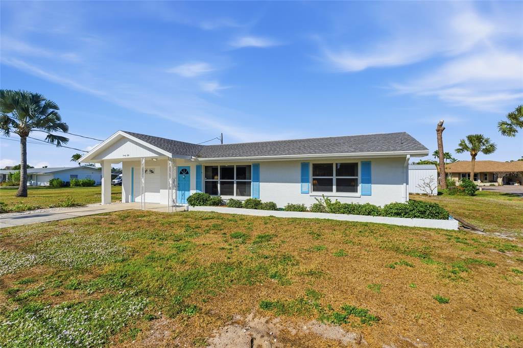 A single-story white house with blue shutters and a covered entryway sits on a lawn — 2050 OYSTER CREEK DRIVE, ENGLEWOOD, FL