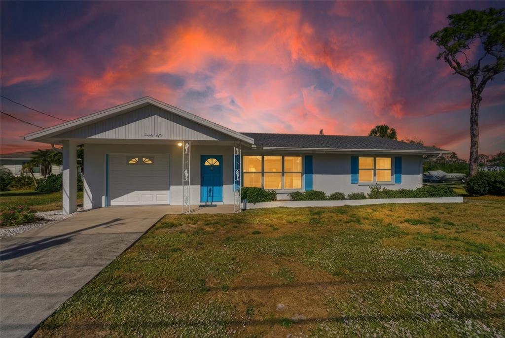 A single-story house with a white exterior, blue door, and attached garage under a sunset — 2050 OYSTER CREEK DRIVE, ENGLEWOOD, FL