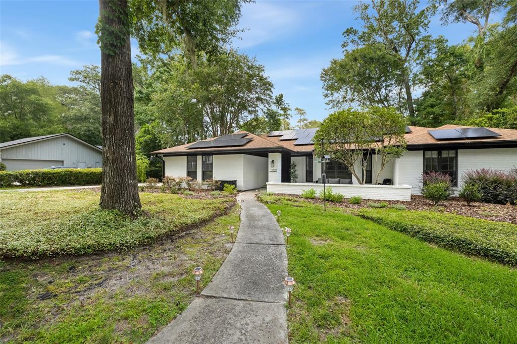 A white brick house with solar panels on the roof and a concrete walkway leading forward — 2322 NW 14TH PLACE, GAINESVILLE, FL