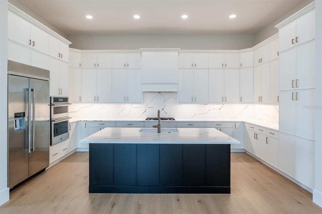 A modern kitchen features white cabinetry, a black island, and marble-style countertops and backsplash — 200 BLUE PEARL CT., SARASOTA, FL