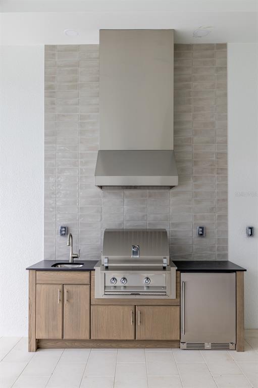 An outdoor kitchen features a stainless steel grill, hood, sink, and refrigerator with tiled backsplash — 200 BLUE PEARL CT., SARASOTA, FL