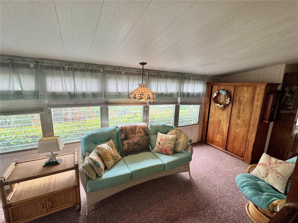 A sunroom features a teal sofa, a rattan side table, and a large wooden cabinet — 616 50TH AVENUE TERRACE W, BRADENTON, FL