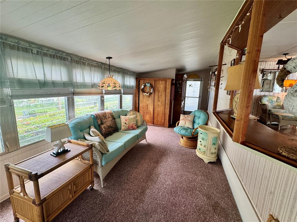 A sunroom features a light blue sofa, wicker furniture, carpeted floors, and large windows — 616 50TH AVENUE TERRACE W, BRADENTON, FL