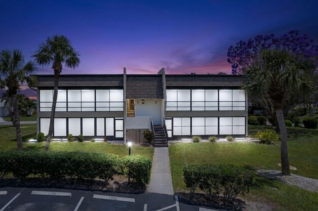 A two-story apartment building with large windows and a central staircase at dusk — 1727 BONITAS CIRCLES UNIT 1718-C, VENICE, FL