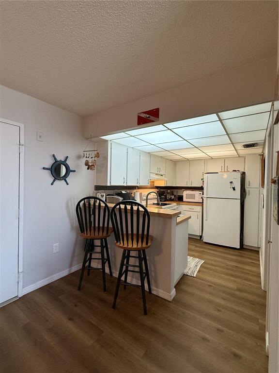 A kitchen with white cabinets, a breakfast bar with two chairs, and wood-look flooring — 3006 CARING WAY UNIT 409, PORT CHARLOTTE, FL