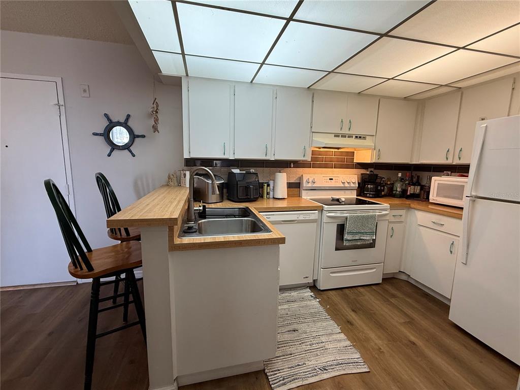 A kitchen features white cabinets, light wood countertops, white appliances, and a drop ceiling — 3006 CARING WAY UNIT 409, PORT CHARLOTTE, FL