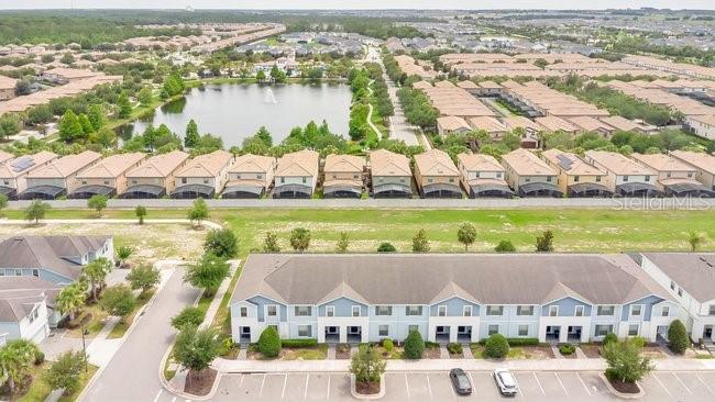An aerial view shows a multi-unit townhouse building with a parking lot and nearby pond — 8904 SYDNEY AVENUE, KISSIMMEE, FL