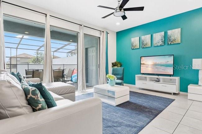 A living room features a teal accent wall, a white sofa, and a large sliding door — 8904 SYDNEY AVENUE, KISSIMMEE, FL