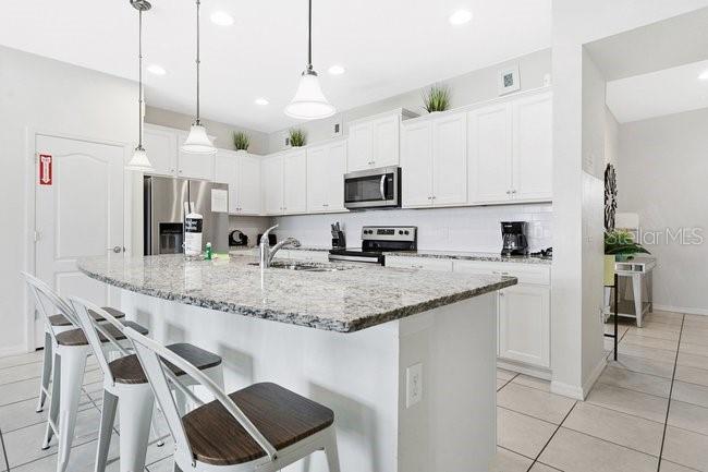 A modern kitchen features white cabinets, granite countertops, a curved island, and three bar stools — 8904 SYDNEY AVENUE, KISSIMMEE, FL