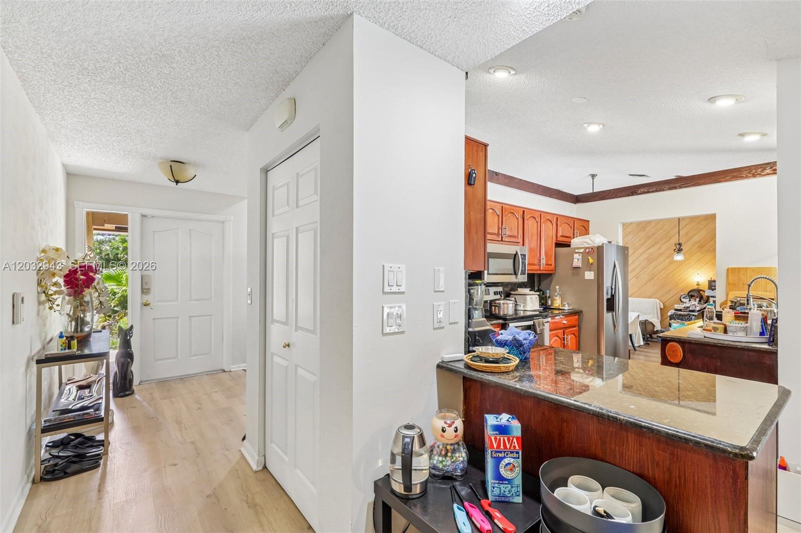 A kitchen with wood cabinets and a granite countertop overlooks an entryway with light flooring — 7160 NW 4th Ave, Boca Raton FL 33487, BOCA RATON, FL