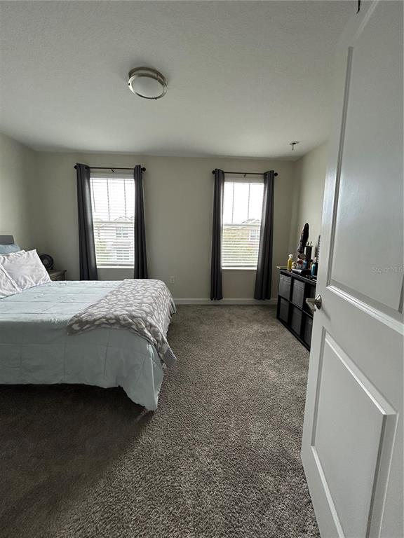 A bedroom features gray carpeting, two windows with dark curtains, and a bed with bedding — 11831 CHARADES STREET, ORLANDO, FL