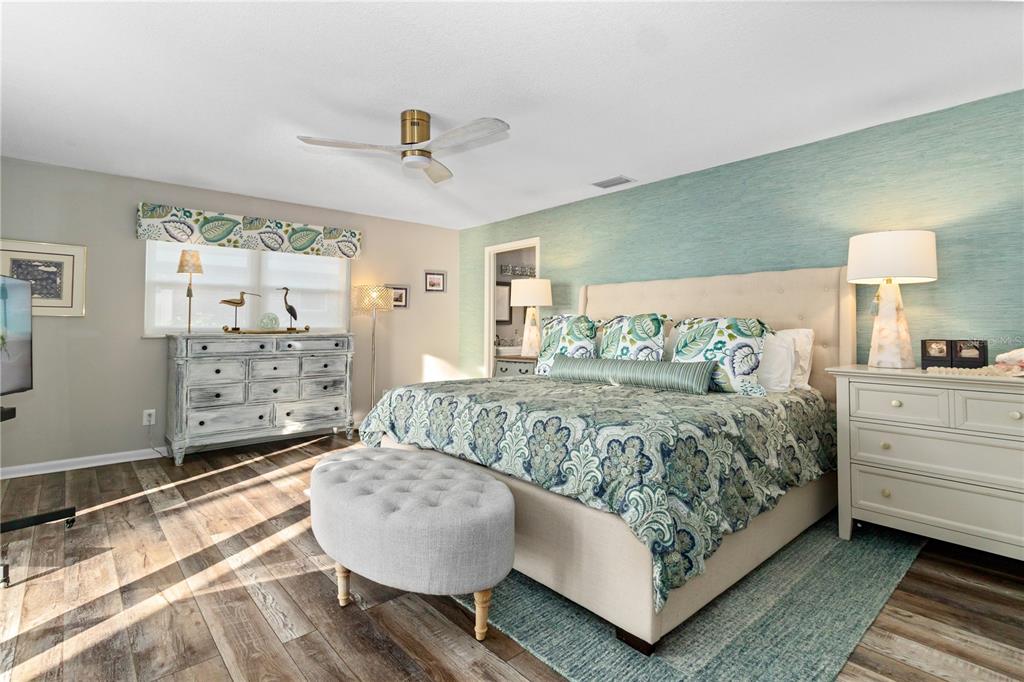 A bedroom features a king bed with patterned bedding, a tufted ottoman, and light wood flooring — 601 LAKE PANSY DRIVE NW, WINTER HAVEN, FL
