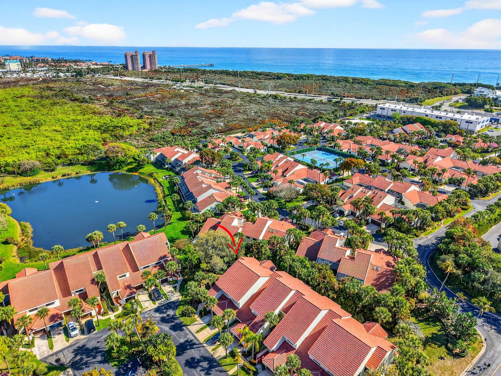 An aerial view shows a residential community with red-tiled roofs near a lake and ocean — 301 Sea Oats Drive # A, Juno Beach FL 33408, JUNO BEACH, FL