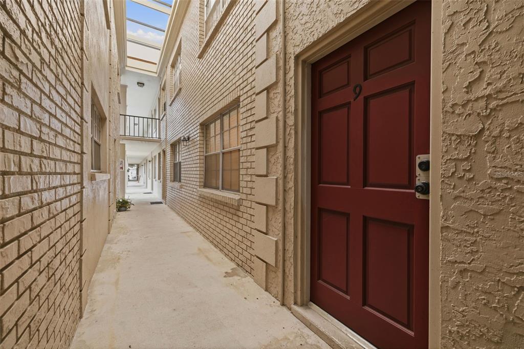 A narrow outdoor walkway with a glass-covered ceiling leads past a red door marked nine — 2207 S CAROLINA AVENUE UNIT 9, TAMPA, FL