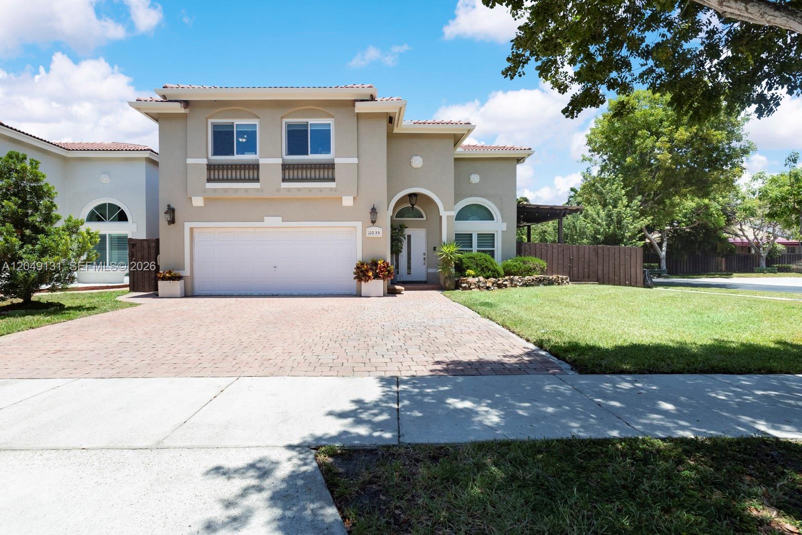 A two-story house features a beige stucco exterior, a brick driveway, and a two-car garage — 11035 NW 47th Ln, Doral FL 33178, DORAL, FL