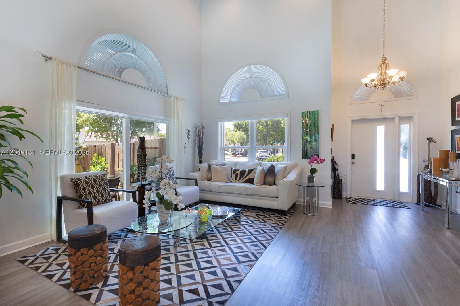 A bright living room features high ceilings, arched windows, a geometric rug, and white furniture — 11035 NW 47th Ln, Doral FL 33178, DORAL, FL