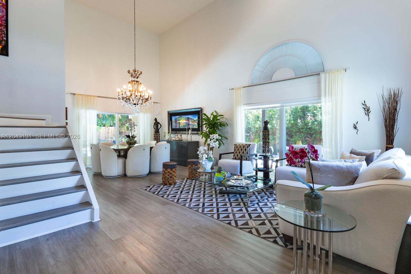 A bright, open-concept living and dining room features high ceilings, wood flooring, and a chandelier — 11035 NW 47th Ln, Doral FL 33178, DORAL, FL