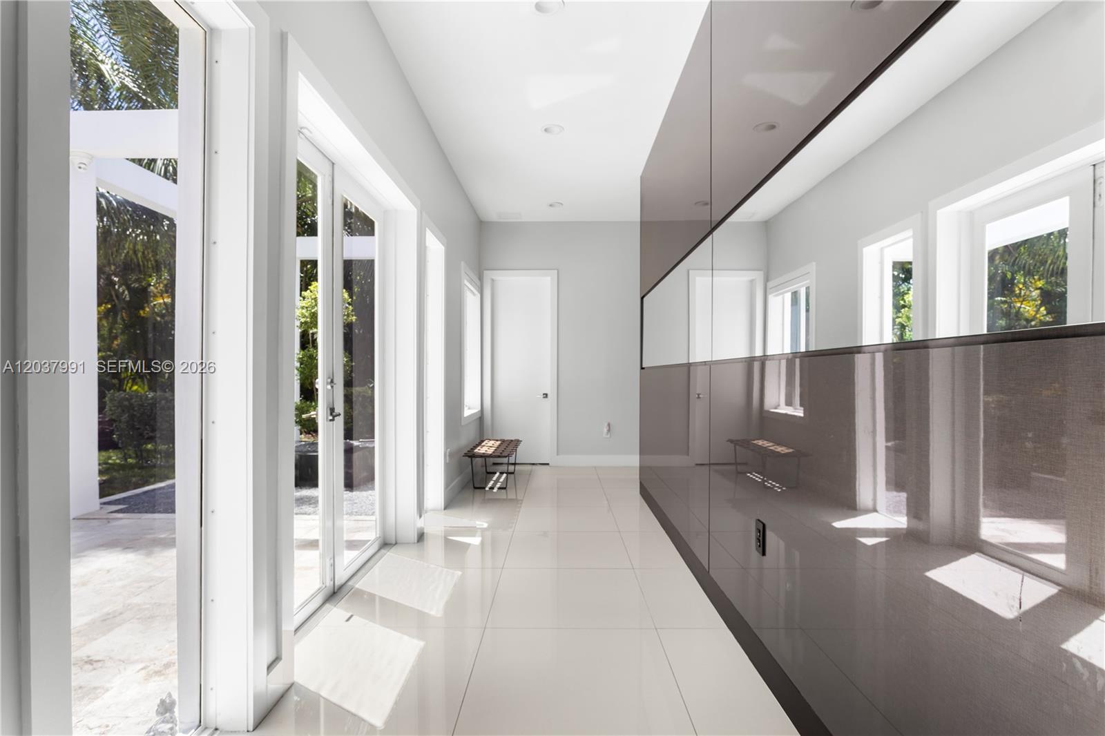 A bright hallway features white tile floors, glass doors, and a large, dark reflective wall panel — 11900 Griffing Blvd, Biscayne Park FL 33161, BISCAYNE PARK, FL