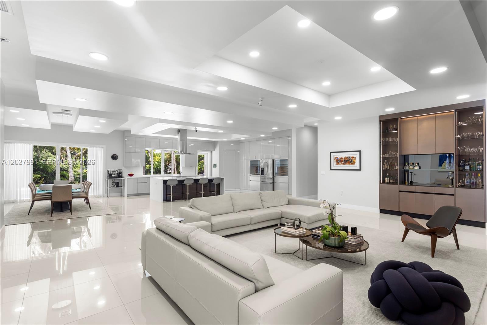 A modern, open-concept living room and kitchen featuring white tile floors and recessed lighting — 11900 Griffing Blvd, Biscayne Park FL 33161, BISCAYNE PARK, FL