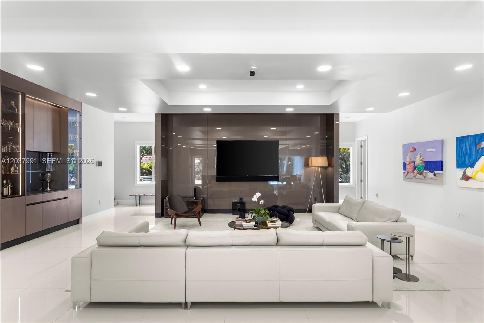A modern living room features a large white sectional, a glossy brown media wall, and recessed lighting — 11900 Griffing Blvd, Biscayne Park FL 33161, BISCAYNE PARK, FL