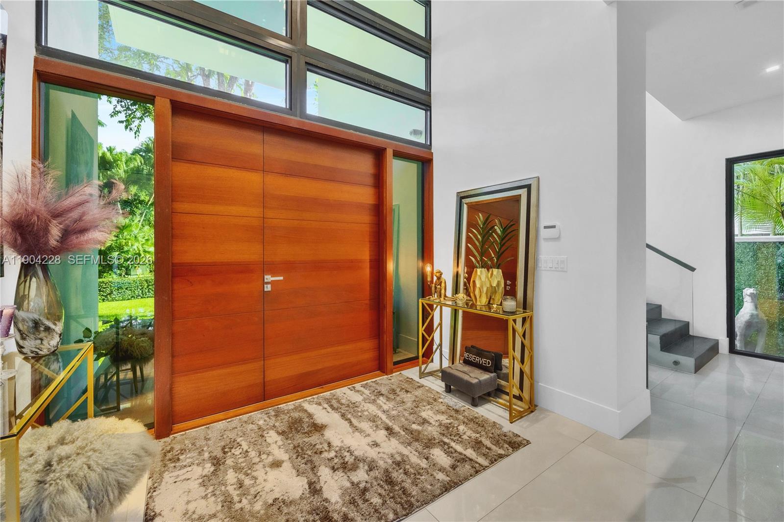 A modern entryway features a large wooden double door, glass panels, and a tiled floor — 3764 Carmen Ct, Miami FL 33133, MIAMI, FL