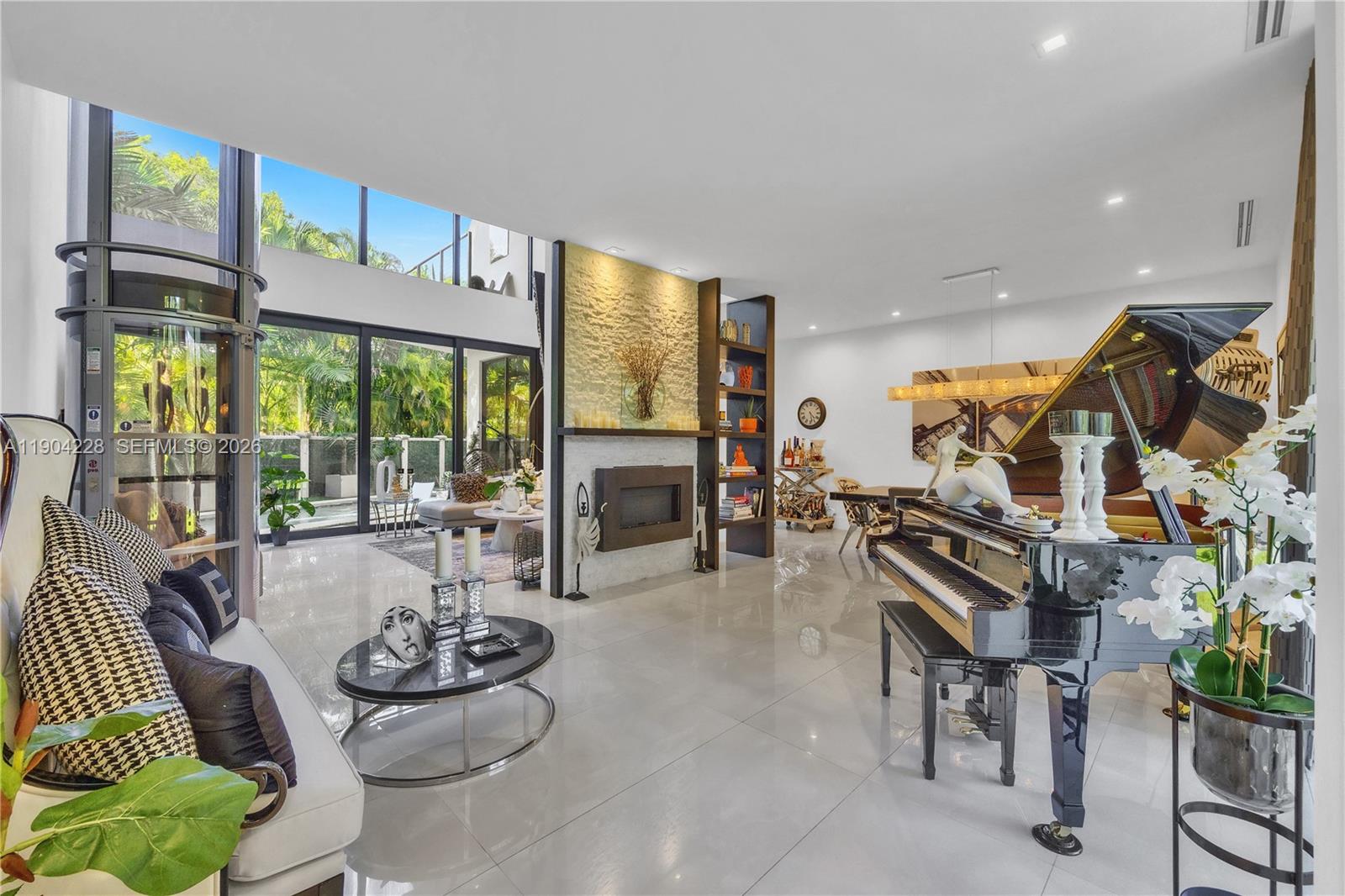 A spacious living room features a grand piano, a fireplace, and floor-to-ceiling windows — 3764 Carmen Ct, Miami FL 33133, MIAMI, FL