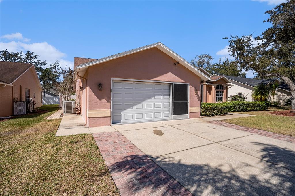 A pink house with a two-car garage and a paved driveway under a blue sky — 7741 DAMASK LANE, NEW PORT RICHEY, FL