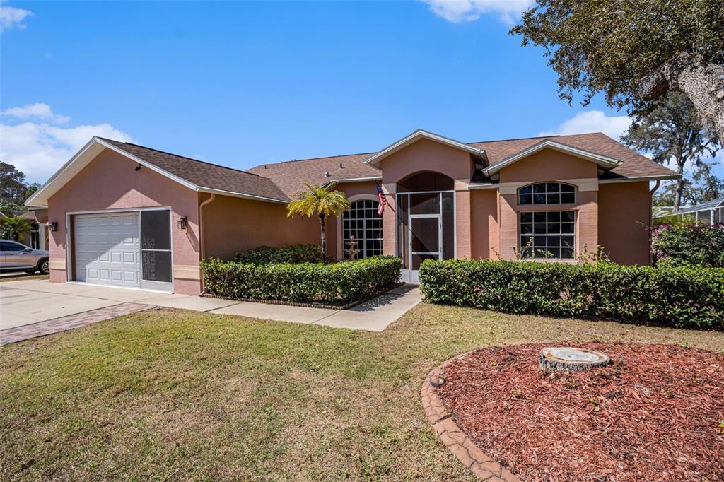 A single-story house with a tan stucco exterior, a two-car garage, and a front porch — 7741 DAMASK LANE, NEW PORT RICHEY, FL