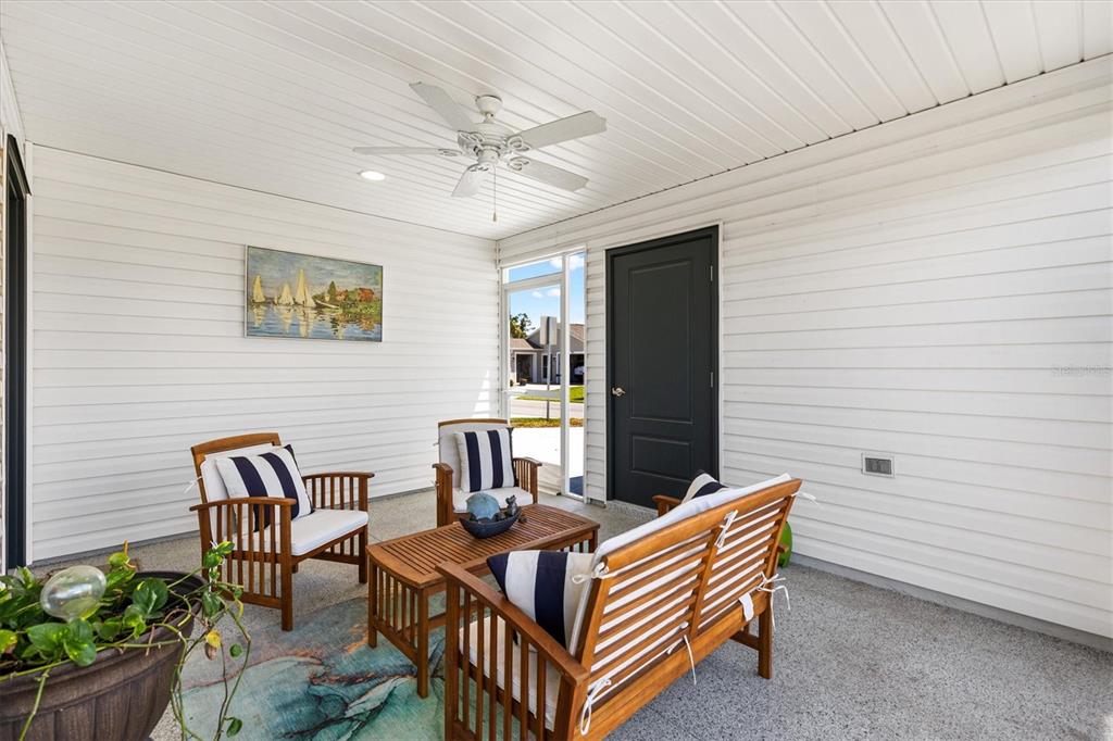 A covered patio features white horizontal siding, a ceiling fan, and wooden patio furniture — 1599 OLIVIA TERRACE, THE VILLAGES, FL