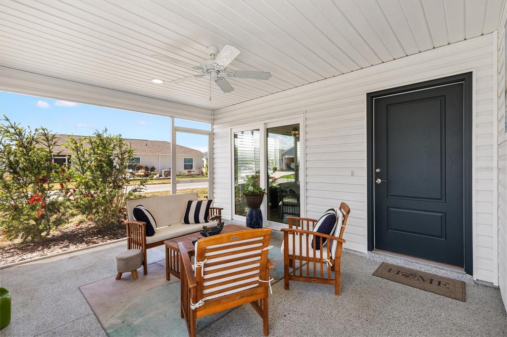 A covered patio features a dark door, outdoor furniture, and a ceiling fan — 1599 OLIVIA TERRACE, THE VILLAGES, FL