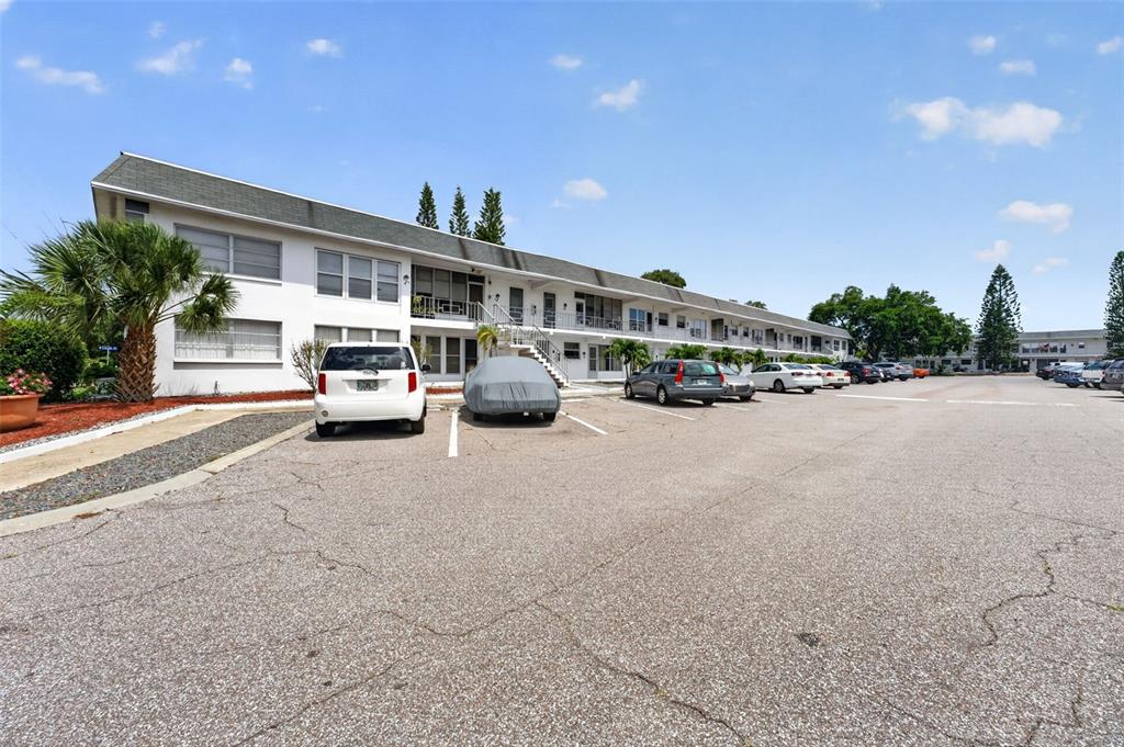 A long, two-story white apartment building sits behind a paved parking lot with several cars — 1221 DREW STREET UNIT A5, CLEARWATER, FL