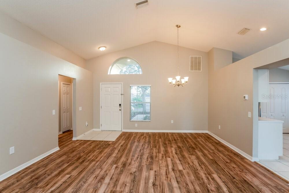 An empty room with vaulted ceilings, wood-look flooring, a chandelier, and a front entryway — 1010 CRISTELLE JEAN DRIVE, RUSKIN, FL