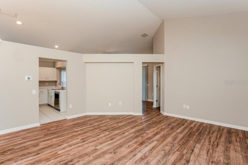 A living room with wood-look flooring, a vaulted ceiling, and an adjacent kitchen — 1010 CRISTELLE JEAN DRIVE, RUSKIN, FL
