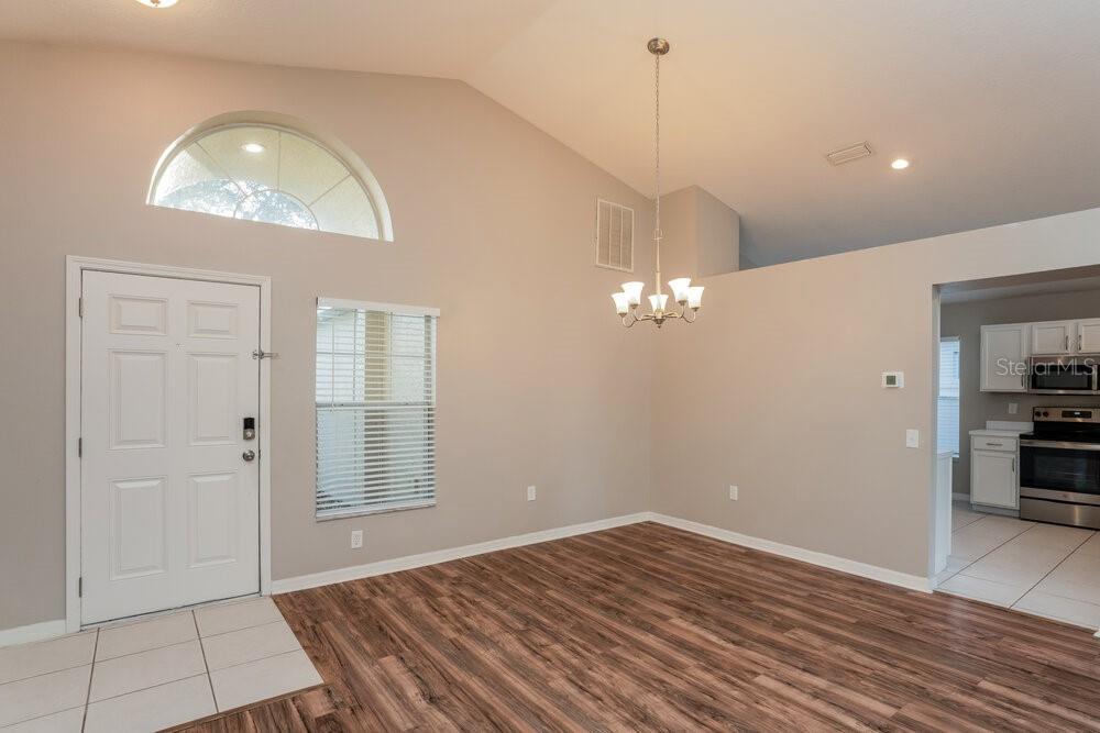 A dining room with vaulted ceilings, wood-look flooring, a chandelier, and an adjacent kitchen — 1010 CRISTELLE JEAN DRIVE, RUSKIN, FL