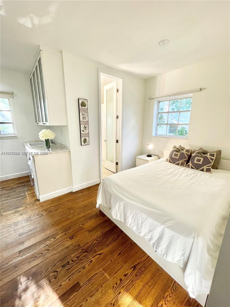 A bedroom features hardwood floors, a white bed, a small kitchenette area, and a doorway — 439 15th St # 18, Miami Beach FL 33139, MIAMI BEACH, FL