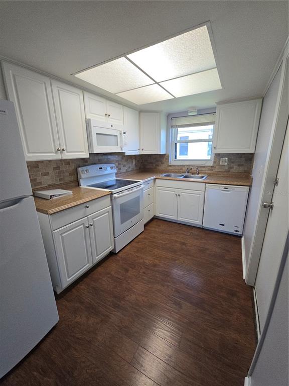 A kitchen features white cabinets, laminate countertops, a tile backsplash, and wood-look flooring — 4924 LIVE OAK CIRCLE UNIT 115, BRADENTON, FL