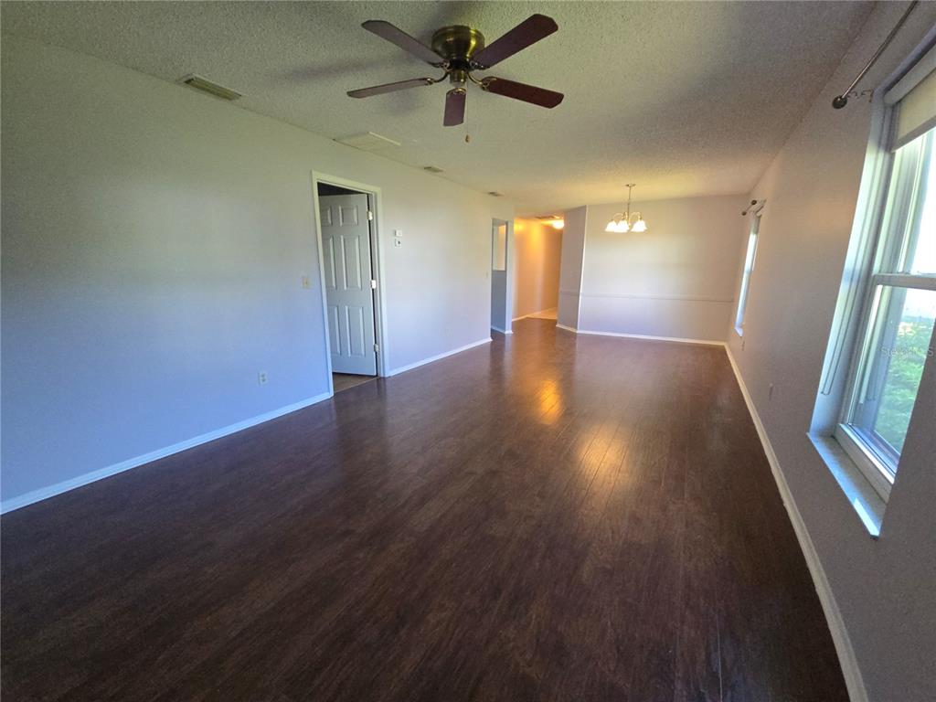 An empty living room features dark wood-look flooring, light gray walls, and a ceiling fan — 4924 LIVE OAK CIRCLE UNIT 115, BRADENTON, FL