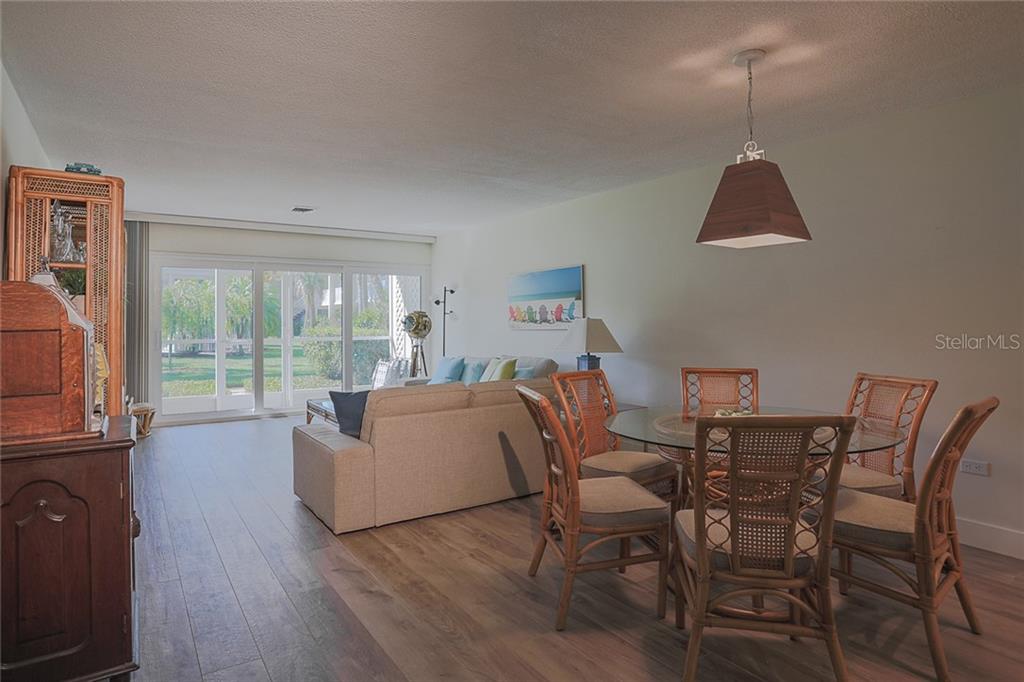 A dining area and living room with wood-look flooring, rattan furniture, and a sliding glass door — 500 S WASHINGTON DRIVE UNIT 16A, SARASOTA, FL