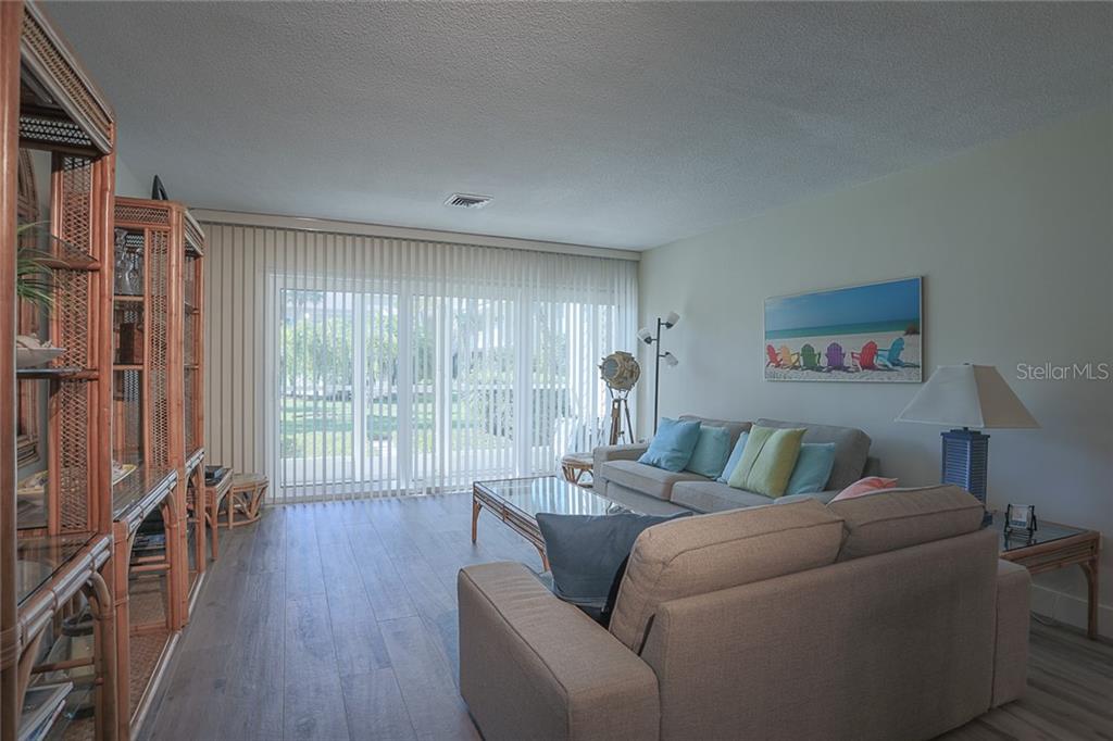 A living room features light wood-look flooring, a beige sofa, and vertical blinds covering sliding doors — 500 S WASHINGTON DRIVE UNIT 16A, SARASOTA, FL