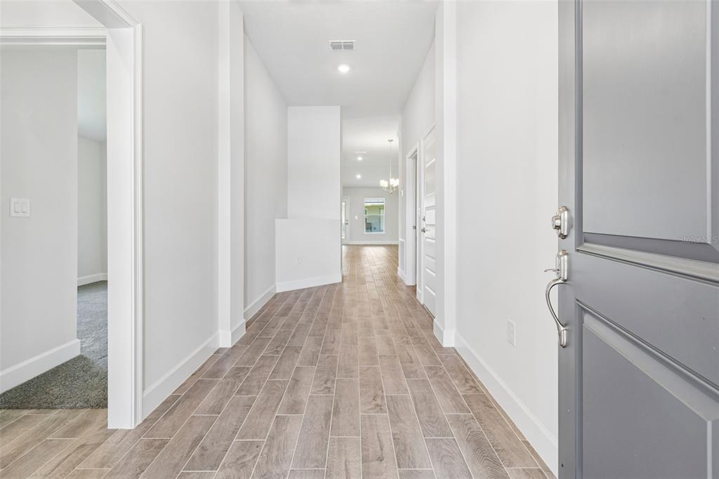 A bright entryway with wood-look tile flooring leads into a hallway with white walls — 12976 KENT BRADLEY STREET, DADE CITY, FL