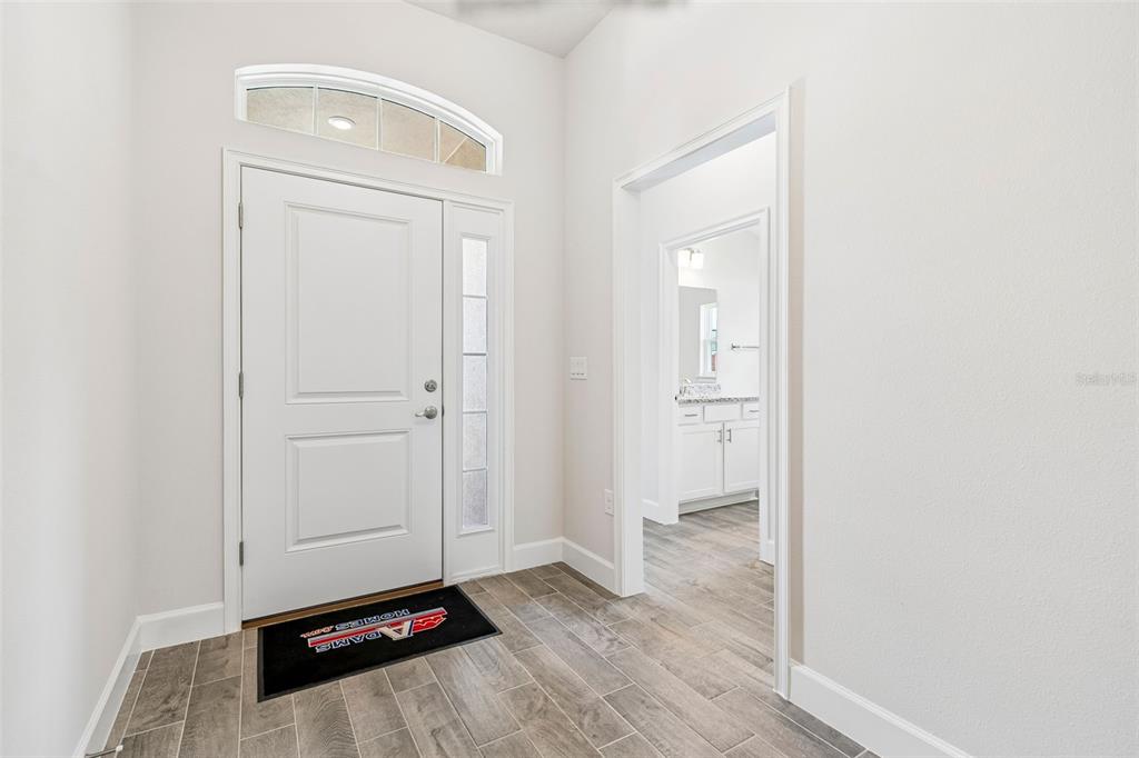 An entryway with tile flooring, a white front door, and a doorway leading to a bathroom — 12976 KENT BRADLEY STREET, DADE CITY, FL