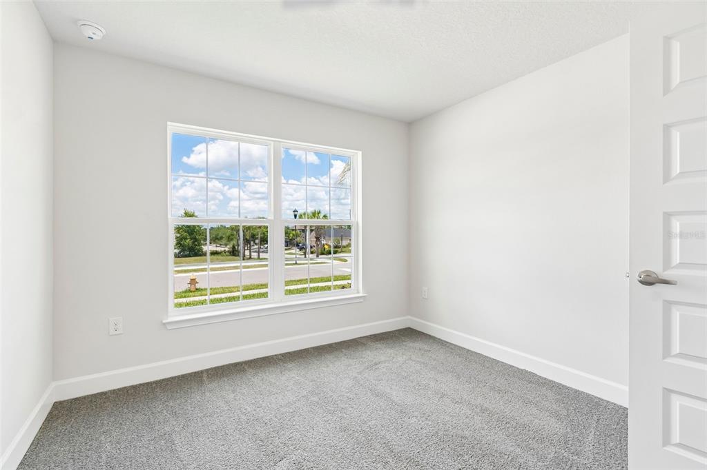 An empty bedroom features gray carpet, white walls, and a window overlooking a street — 12976 KENT BRADLEY STREET, DADE CITY, FL