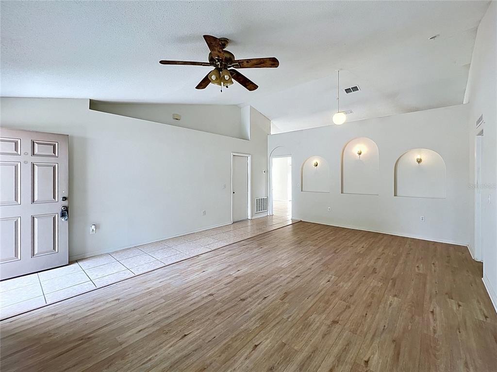 An open living room features wood-look flooring, a vaulted ceiling, and three arched wall niches — 6004 KALEY DRIVE, WINTER HAVEN, FL